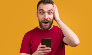 Excited,Surprised,Man,With,Phone,In,Hands,Holding,His,Head