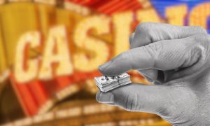 Image of hand holding small money in front of casino sign for story on the impact beyond revenue the workers' strike is having on Detroit casinos