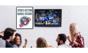 Sports fans watching the Detroit Lions on TV. There is a poster on the wall with a Michigan logo and the words "Sports Betting Handle Record" to signify Michigan setting a record in November 2023.