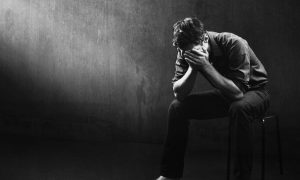 Black and white image of a man sitting alone in a bare room, his face in his hands. The Problem Gambling Symposium found awareness and treatment options lacking in Michigan as gambling continues to expand online.