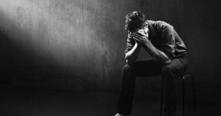 Black and white image of a man sitting alone in a bare room, his face in his hands. The Problem Gambling Symposium found awareness and treatment options lacking in Michigan as gambling continues to expand online.