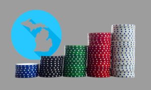 In front of a grey background with a blue outline of the state of Michigan, large stacks of casino chips grow with each progressive stack. Michigan's online casinos have shown revenue growth each month compared to the same month a year prior, up at least $19 million each time.