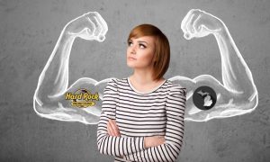 Woman stands in front of a way with a drawing of two huge arm muscles. On one bicep is the logo for Hard Rock online casino. On the other bicep is the out of the state of Michigan. The arrival of a Hard Rock online casino can make Michigan's market even stronger, based off the operator's performance in New Jersey.