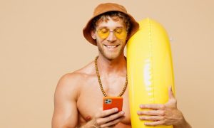 Man in swimsuit is holding an inner tube and looking at his phone. Michigan online casino revenue topped $191.4 million in July, up 25% year-over-year. The sector is on pace for a record $2.32 billion in '24.