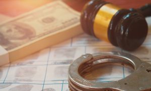 A picture of some money, a judge's gavel and a pair of handcutffs