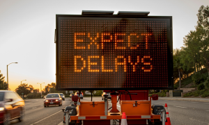 Expect delays road sign in front of heavy traffic
