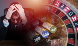 a person with their head in their hands next to a roulette wheel and chips