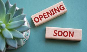 a pair of tiles spelling opening soon next to a plant
